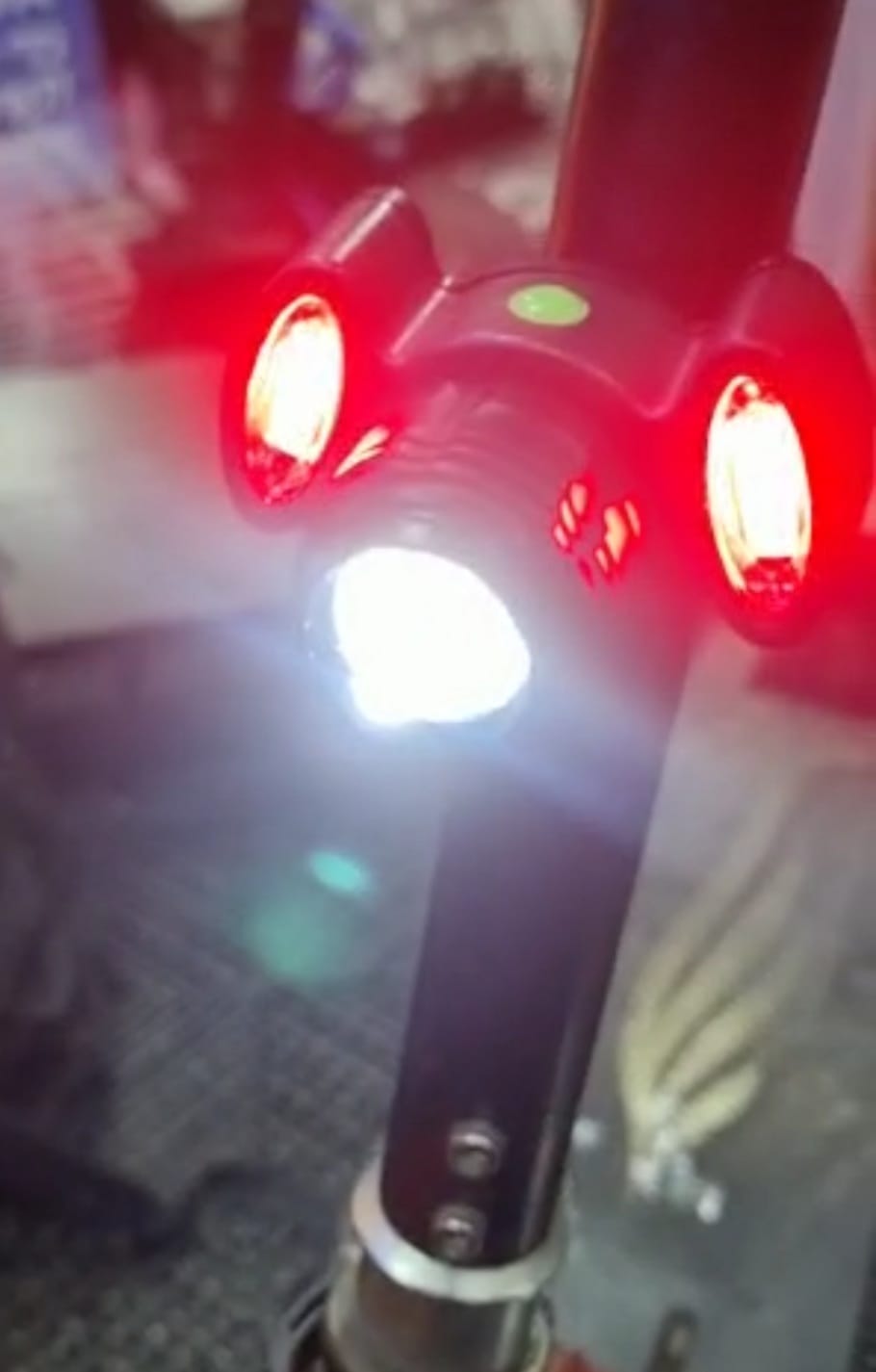 פנס לבן באמצע ושני פנסים אדומים בכל צד עם מספגרת שחורה מותקן על קורקינט